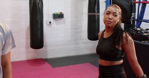 Asian trainee practicing jab with hispanic coach holding mitts in boxing gym training