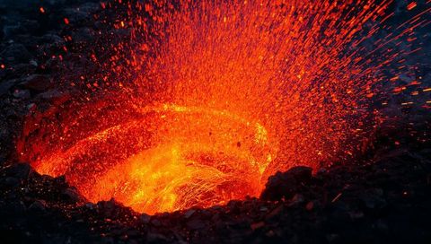 Molten lava fountain eruption in volcanic crater at night
