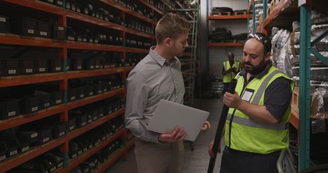 Caucasian businessman reviews inventory with a worker in a warehouse. Their collaboration ensures efficient stock management and workplace synergy.