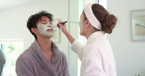 Asian man and african american woman applying facial mask together during skincare routine