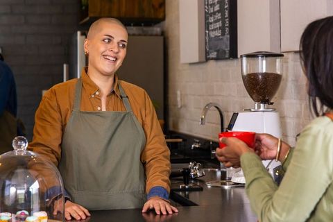 Smiling barista serving coffee and chatting with customer at modern cafe counter