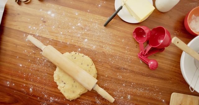 This image displays a top-down view of a wooden table covered with various baking utensils, cookie dough, and flour. The rolling pin is on the dough, ready to be used. Ideal for showcasing home baking, recipes, and kitchen themes. Perfect for cooking blogs, culinary websites, and DIY baking tutorials.