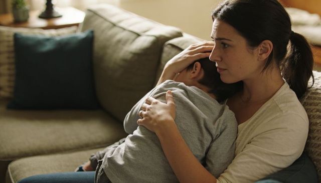 Mother comforting son on sofa, hugging and soothing during tender home moment