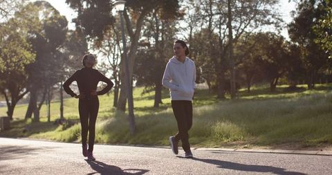 African American Woman and Young Man Walking in Sunlit Park Wearing Hoodies and Activewear