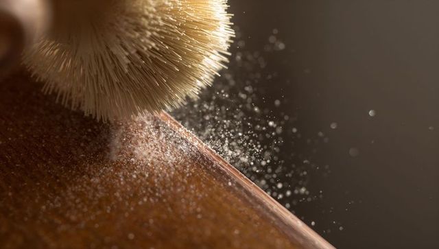 Natural bristle brush sweeping dust from wood table edge with powder bokeh macro