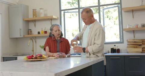 Senior asian couple pouring water at marble island in sunlit modern kitchen sharing quiet moment