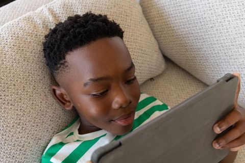 African american boy relaxing on couch using tablet for learning and entertainment