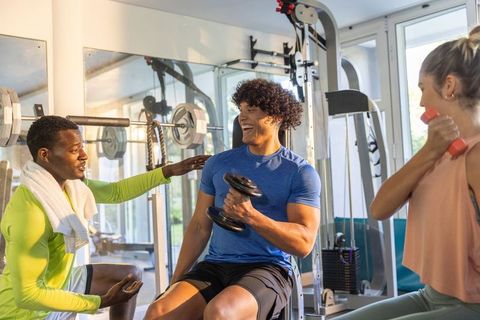 Diverse personal trainer coaching group lifting dumbbells in bright gym promoting teamwork