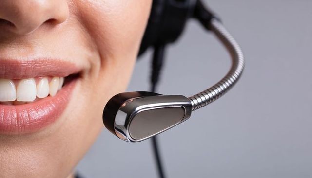 Closeup smiling customer service agent speaking into sleek metal headset microphone