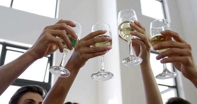 People toasting with white wine glasses, conveying themes of celebration, friendship, and special occasions. Perfect for usage in promotional materials for parties, social events, and advertisements for wine brands or festive gatherings.
