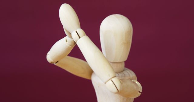 Wooden art mannequin raising arms in a defensive gesture against a solid red background. Can be used for illustrating concepts of emotion, defense, protection, arts and crafts, artistic modeling, expressive poses, and educational purposes.