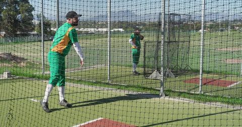 Cricket bowlers practicing in netted outdoor training cage on sunny turf field