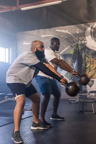 Two african men training with kettlebells in industrial gym featuring graffiti wall