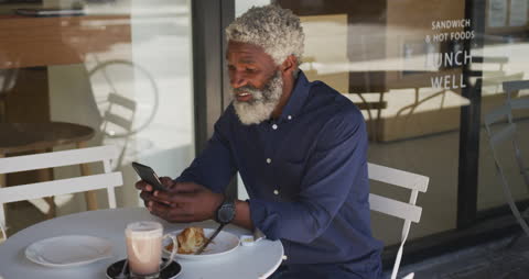 Senior Man Relaxing at Outdoor Cafe Using Smartphone