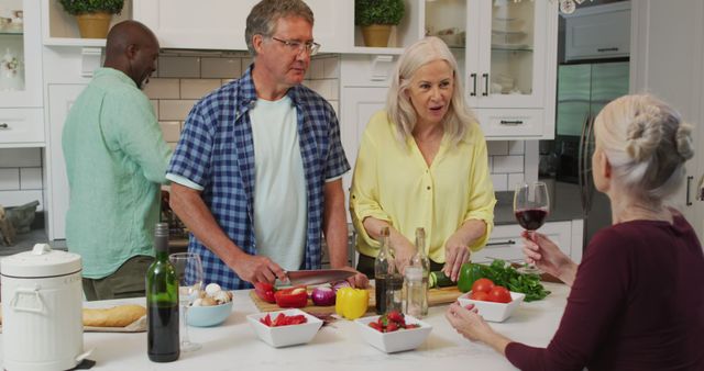 Group of seniors cooking meal together in modern kitchen, enjoying each other's company. Two men chopping vegetables while two women chatting and holding wine. Perfect for showcasing active lifestyle of older adults, community, and family gatherings.