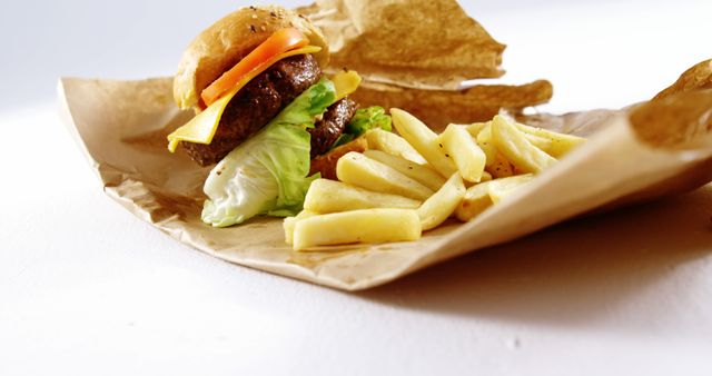 A cheeseburger is paired with a side of fries and chips, presented on a simple paper wrapping. The image captures a classic fast-food meal, evoking a casual dining experience.