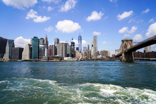 Perfect for travel advertisements, tourism brochures, and articles about New York City. Highlights iconic skyline with Brooklyn Bridge over Hudson River, showcasing landmarks and water activity. Great for educational content, city guides, and promotional materials.