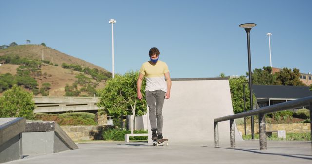 Caucasian man wearing face mask, riding and jumping on skateboard on sunny day - Download Free Stock Photos Pikwizard.com