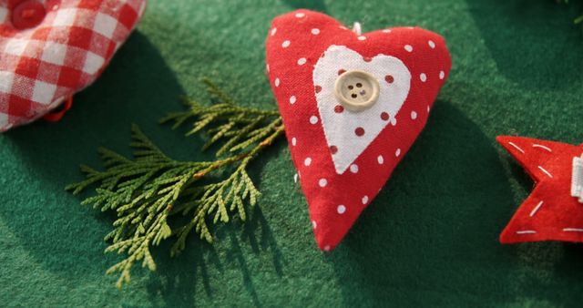 A handmade red heart with a button detail is featured prominently on a green background, with copy space. Its festive appearance suggests it could be part of a Christmas decoration or a craft project.