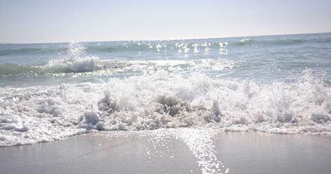 Foamy Waves Crashing on Sunny Sandy Beach with Blue Sky