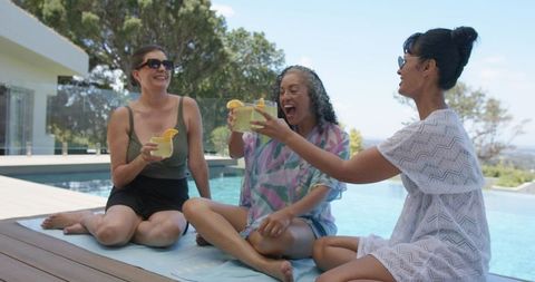 Chic friends toasting poolside with cocktails laughing and relaxing on sunny summer deck
