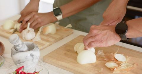 Couple chopping onions and peeling garlic on kitchen counter while wearing smartwatches