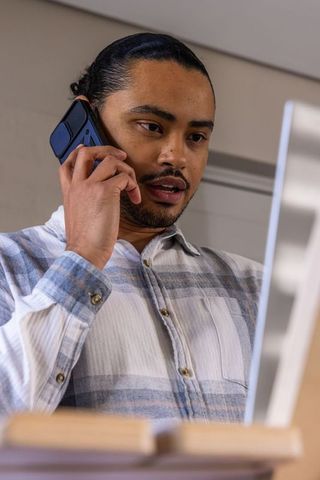 Asian professional talking on smartphone while checking monitor at modern home office desk