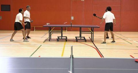 Male Team Engaging in Doubles Table Tennis in Indoor Sports Hall