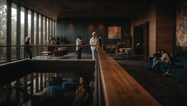 Woman in white headwrap leaning on mezzanine railing in modern two-story lounge