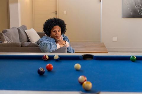 Thoughtful african american man in 20s leaning on sofa watching blue pool table in lounge