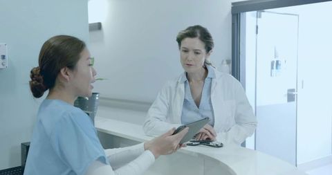 Female Doctor and Nurse Reviewing Patient Records at Clinic Reception Desk