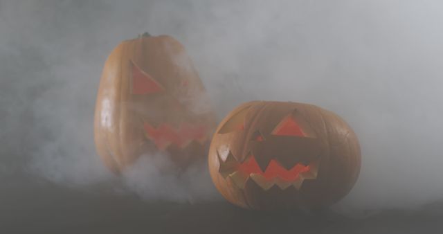 Smoke effect over two scary face carved halloween pumpkin against grey background. halloween holiday and celebration concept