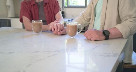 Senior couple holding hands over kitchen island with coffee mugs and warm morning light