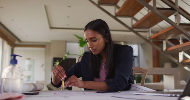 Female architect preparing blueprints at a desk in a modern home office with a wooden staircase in the background. Ideal for illustrating female professionals, home offices, architectural design, and focused work environments.