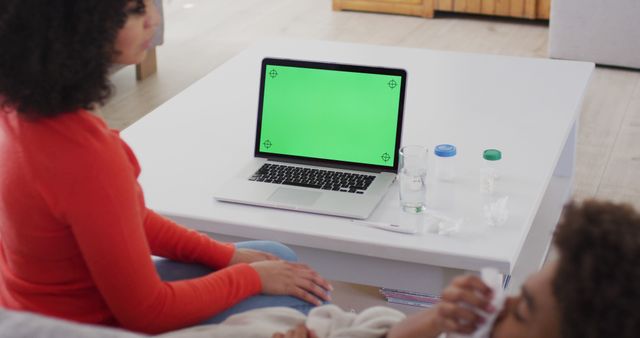 Mother and child sitting in living room looking at laptop with green screen, implying interaction with technology or watching media. Suitable for themes around parental involvement, screen time, family bonding, and home activities. Ideal for blogs about technology usage in family settings, educational materials, parenting websites, and promotional content for film and design backgrounds.