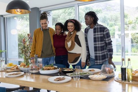 African American friends sharing meal and smiling around long wooden table in modern home