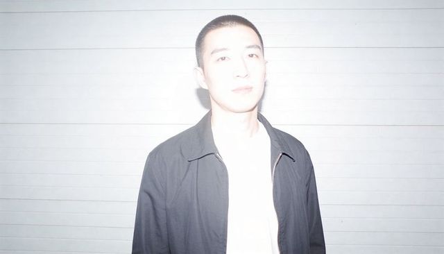 High-key portrait of asian man wearing dark zip jacket and white tee against slatted wall