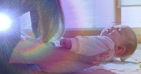 Sunlit mother cradling newborn on arms with lens flare and soft foam play mat