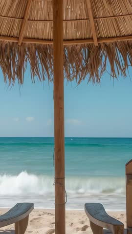 Vertical beach video with waves rolling, straw umbrella swaying above lounge chairs