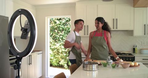 African American couple filming and cooking at kitchen island with ring light