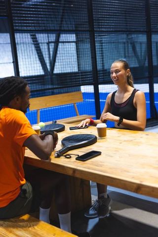 Diverse Friends Relaxing at Padel Court Table After Match