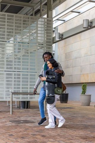 Walking and embracing urban skateboard couple in covered courtyard using phone