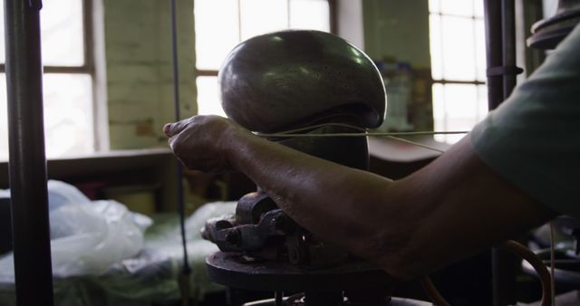 Craftsman in workshop forming a helmet using industrial equipment. Perfect for illustrating traditional manufacturing processes, metalworking techniques, or artisan skills. Can be used in articles, websites, or publications focusing on craftsmanship, industrial work, and manual labor jobs.