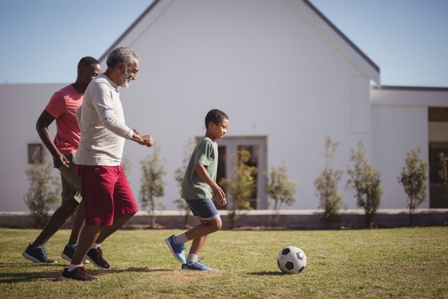Boy playing football with his father and grandson in garden