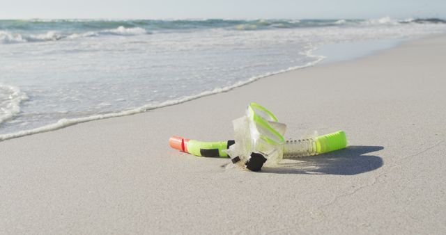 Snorkel gear lying on sandy beach near ocean waves. This scene is ideal for promoting beach vacations, summer holidays, and leisure activities. It can be used in travel advertisements, beach resort brochures, and marine sports promotions. The bright, sunny atmosphere suggests a warm, inviting destination perfect for relaxation and fun.
