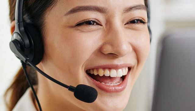 Laughing Asian customer support representative wearing headset and smiling toward laptop