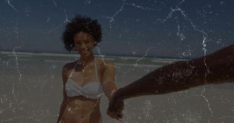 Holding hands on sunny beach woman leading partner while smiling in white bikini