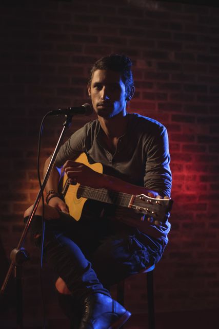 Confident male singer performing with guitar in a nightclub, illuminated by colorful stage lights. Ideal for use in promotions for live music events, nightclub advertisements, musician profiles, and entertainment industry marketing materials.