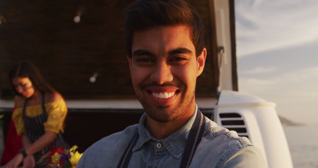 Smiling man in apron posing while a woman arranging flowers in the background - Download Free Stock Images Pikwizard.com