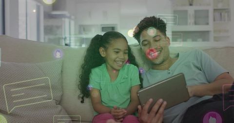 Father and daughter smiling using tablet with social chat overlays on couch